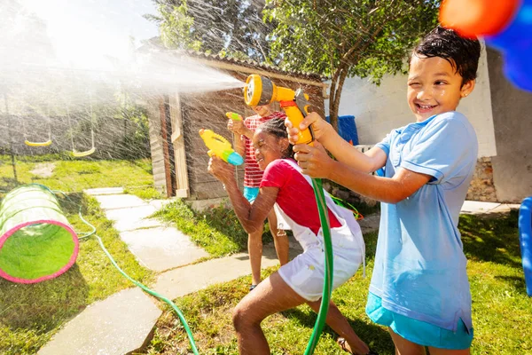 Fun active game of water gun fight with boy showing grimace strong expression holding garden hose sprayer