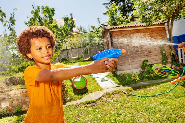 可愛いです幸せな男の子とともに巻き毛と黄色のTシャツ撮影水銃でゲームで友人に対して — ストック写真