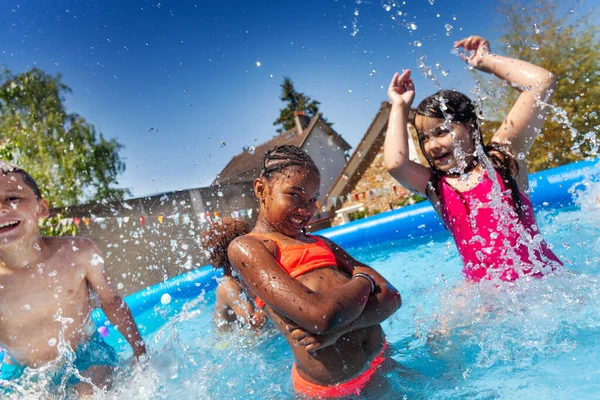 子供たちの幸せなグループは 2人の女の子が水をはねながらインフレータブルプールで遊ぶ — ストック写真