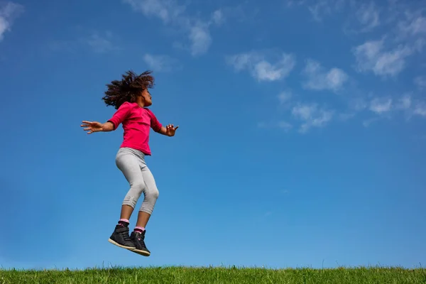 快乐的小女孩 卷曲的头发在蓝天上跳跃 在草地的侧面看云彩 — 图库照片