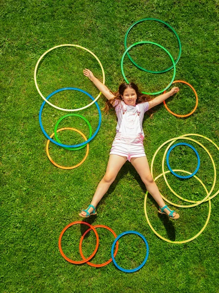 美丽的白人小女孩躺在草地上 地上挂着许多五彩缤纷的呼啦圈 — 图库照片