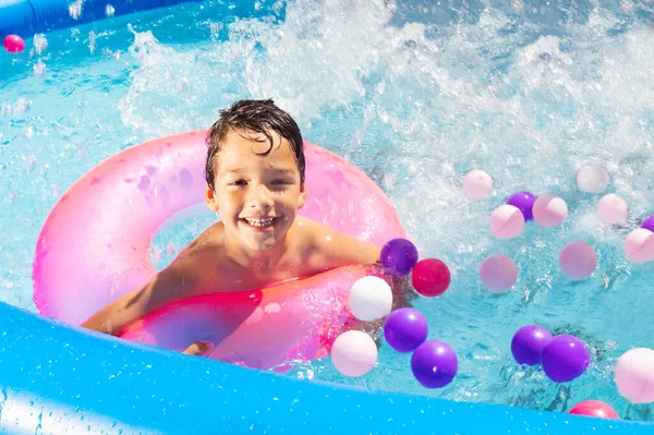 快乐的男孩在游泳池里玩耍 头顶着浮标 飞溅着彩球 — 图库照片