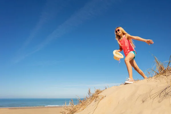 砂浜の近くの砂丘の上の少女の肖像歩くとわら夏の帽子を保持 — ストック写真