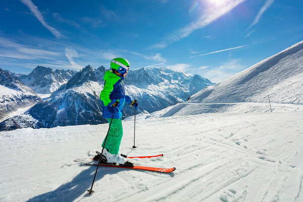 Портрет из-за маленького мальчика стоять на склоне горной тропы горнолыжный путь носить шлем и маску позируя над высоким снежным пиком
