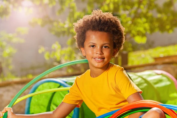 一个快乐的黑人男孩坐在草坪上 戴着呼啦圈 面带微笑 他的近照 — 图库照片