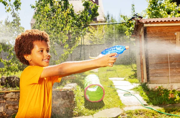 笑顔子供の男の子とともに巻き毛と黄色のTシャツ撃ち水銃でゲームで友人に対して — ストック写真