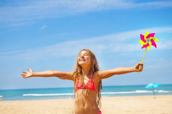 笑顔の女の子の幸せな肖像画でピンホイールと広い広がり手立って海のビーチ目を閉じて見て — ストック写真