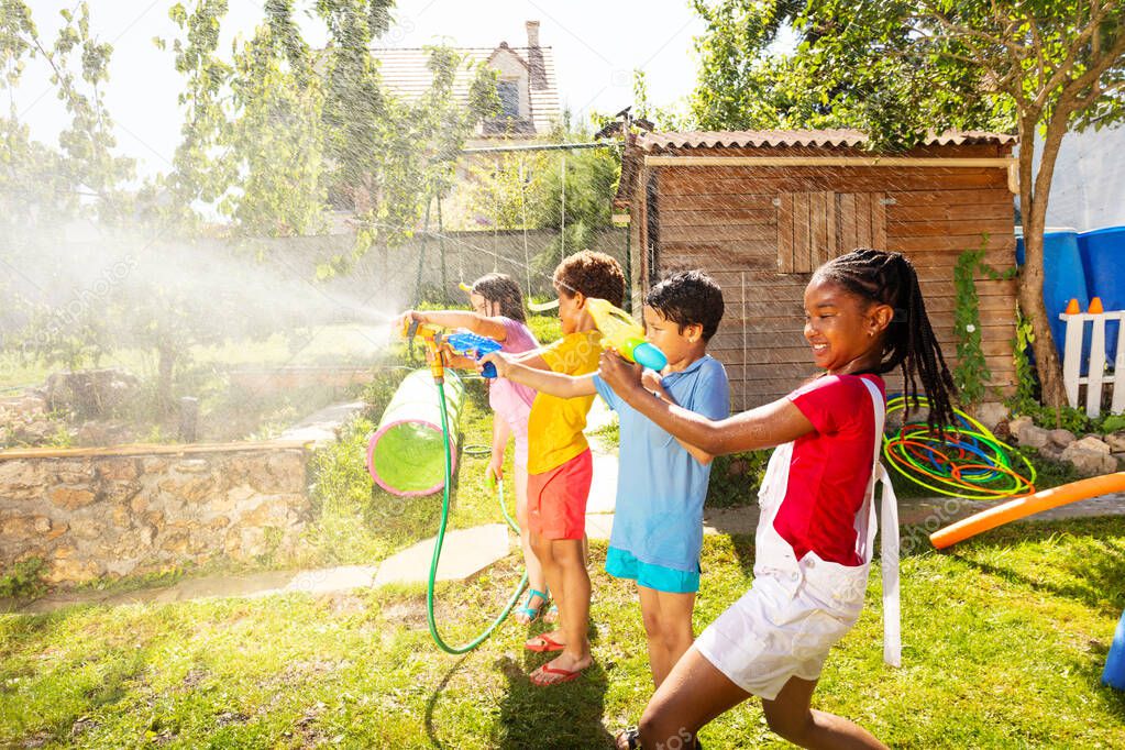 Children in the middle of water gun fight shooting guns, pistols and garden hose sprinkler