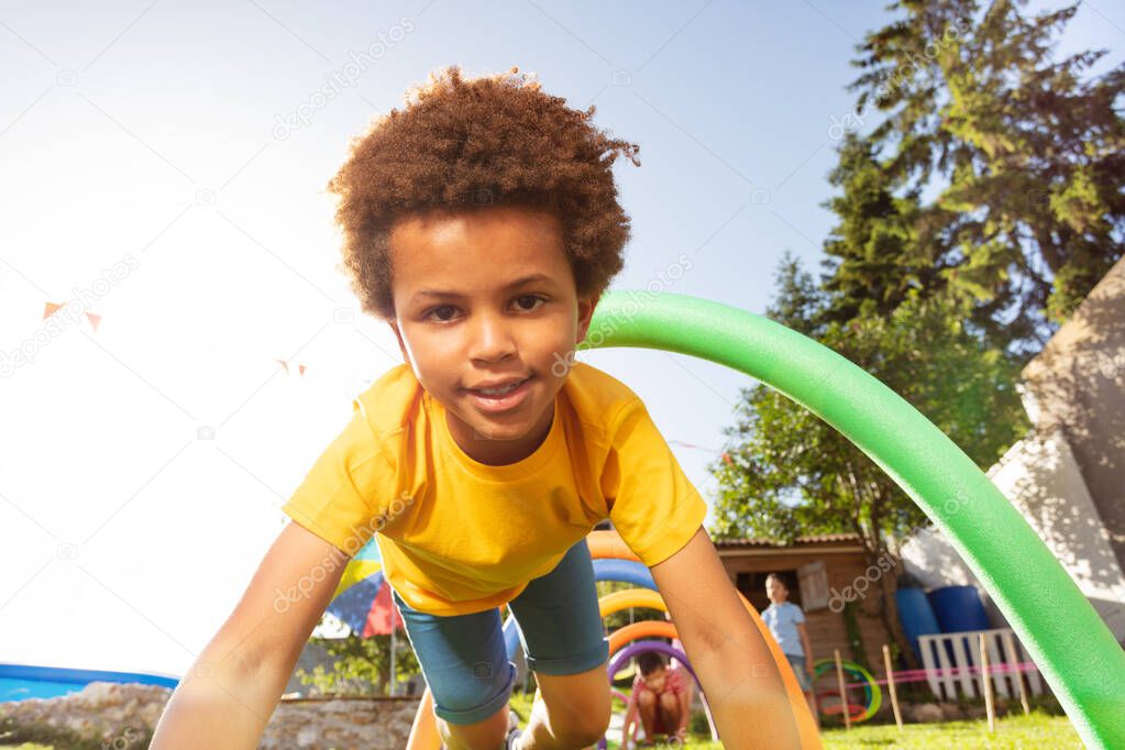 Portrait of nice black boy passing tunnel made of arcs on backyard playground