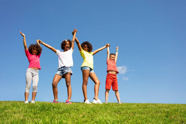 Group of diverse looking children stand on the grass in the park calm happy and lifting hands together