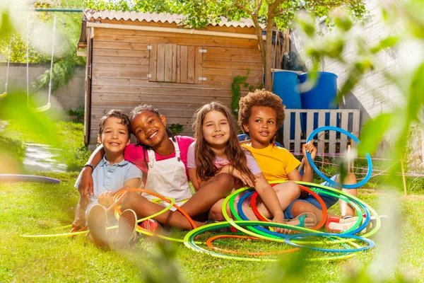 4人の子供の男の子のグループは 女の子が一緒に暑い夏の日に笑みを浮かべて抱擁フラフープを保持座っている — ストック写真