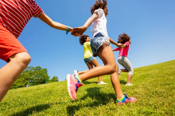 Profile view of kids run and pull each other in the park holding hands focus on legs