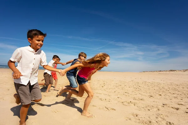 子供たちのグループ男の子と女の子は一緒に手を取り合ってビーチで楽しみのために速く走ります — ストック写真