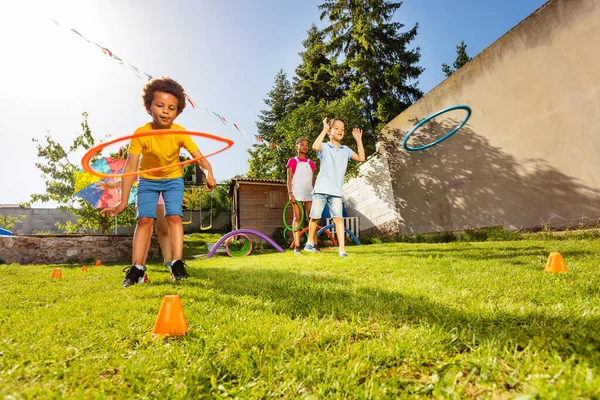 Group of friends play with color sport hoops, black boy jumps inside hold by two kids