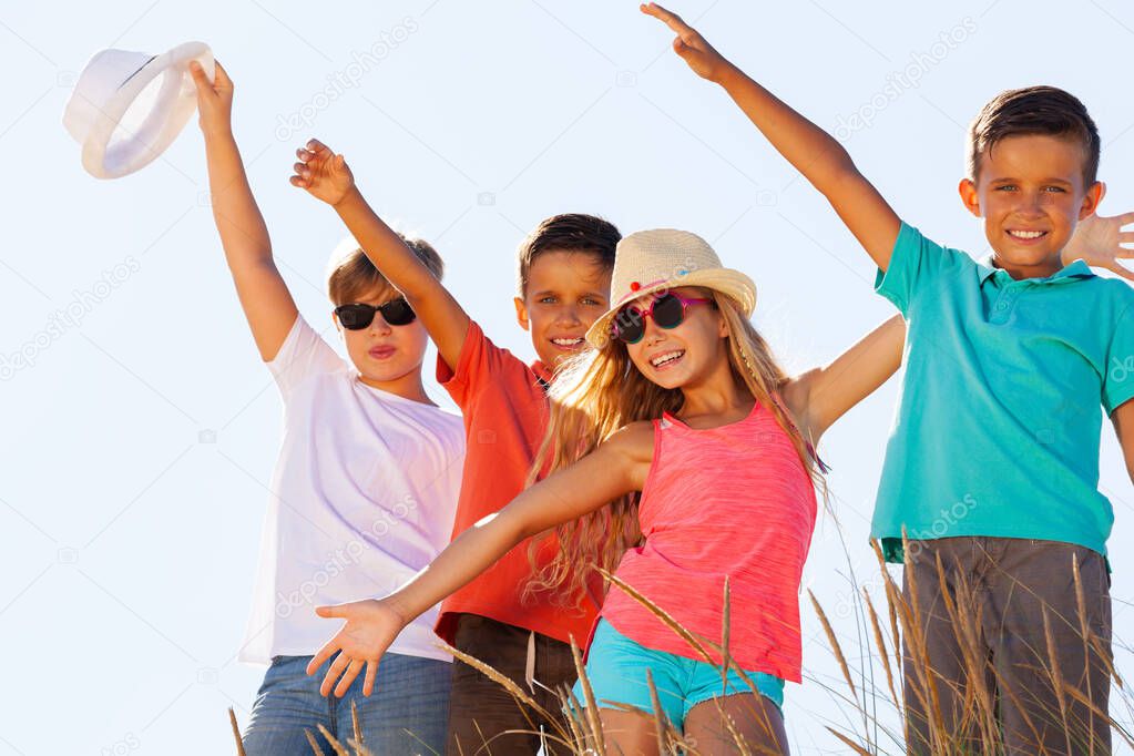 Group of happy kids in summer casual closes wave hands over blue sky standing together