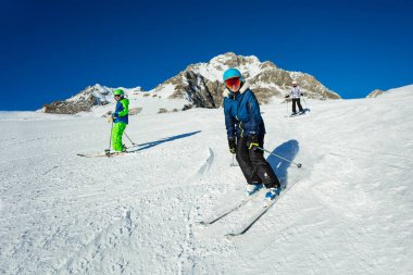 Bir grup çocuk ve genç arkadaş portresiyle tepede kayak yapıyor. Güneşli bir gün Alp Dağları tatil köyünde.