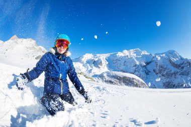 Mavi elbiseli ve aynalı turuncu gözlüklü mutlu genç kız portresi güzel dağların üzerinden havaya kar fırlatıyor.
