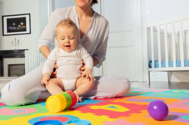 Genç anne, çocuk odasında yerde oturmuş bebekle oyun oynuyor ve etkileşime geçiyor.