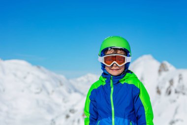 Spor kasklı, kayaklı ya da snowboard gözlüklü bir çocuğun portresi arkaplandaki parlak, güneşli dağ tepelerinde.