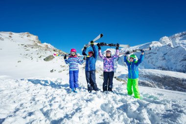 Kayak tatili portresi. Birçok çocuk spor malzemelerini havaya kaldırıyor. Gülümsüyor, renk gözlüğü ve miğfer takıyor.