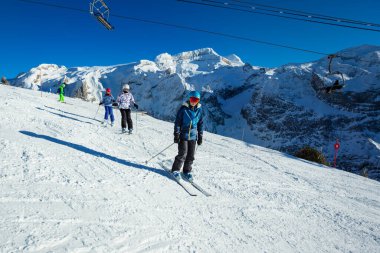 Dört çocuk Alp yamacında kayak yapıyor. Okul düzeninde birbiri ardına kameraya doğru ilerliyorlar.