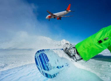 Dağlık tepelere bağlı snowboard 'u ve gökyüzündeki ticari jet uçağını kapatın. Kayak tatili konseptini resmediyorlar.