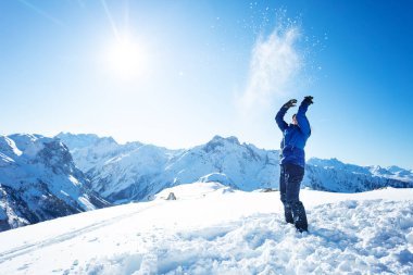 Genç bir kızın yan portresi arka plandaki dağ zirvelerinin üzerinden havaya kar atıyor.