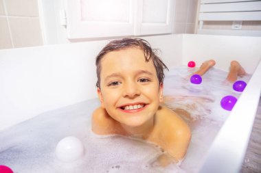 Bir çocuğun portresi evde banyo suyunda oyuncaklar ve sabunla oynuyor.
