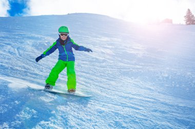 Snowboard 'dan aşağıya doğru hızla inen bir çocuğun el ve kar tozu güneşiyle dengelenmiş bir fotoğrafı.