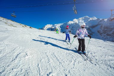Üç çocuk okul grubunun bir parçası olarak Alp yamacında kayak yapıyor. Birbiri ardına dağlar ve arka planda kaldırma.