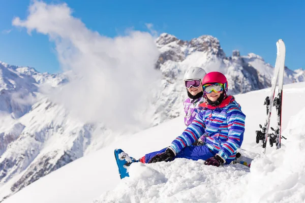 二人の幸せな女の子が高いピークと雪の中で雲の上にスキーで山の中に座ってカメラを見て笑顔 — ストック写真