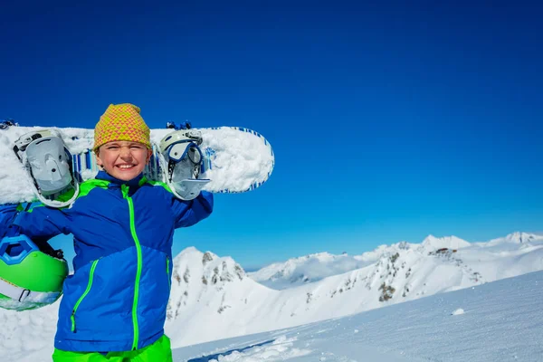 天気の良い日には 山のパノラマの上の肩の上にスノーボードやカジュアルな帽子を保持する少年の近くの肖像画 — ストック写真