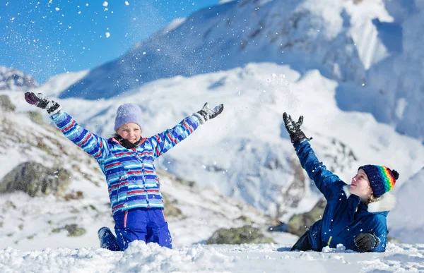 两个可爱的女孩一起坐在地上玩乐 在美丽的山上向空中扔雪 — 图库照片