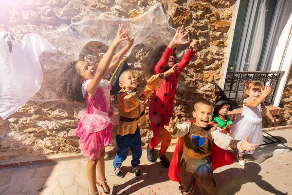 一群孩子举起手 伸手去拿糖果 他们穿着万圣节服装站在墙边 墙上挂着鬼魂 — 图库照片