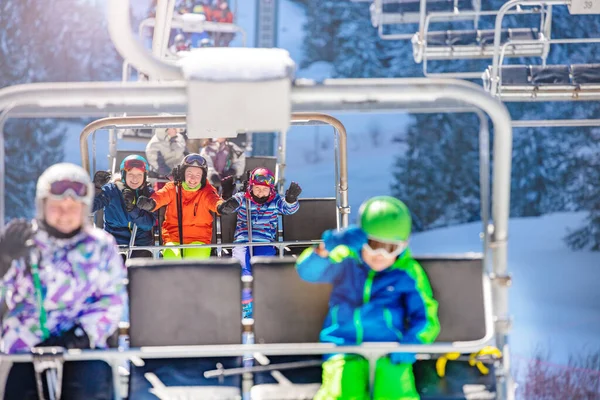 多くの子供たちは山のリゾートでスキーリフトで別の椅子に座って手を振って — ストック写真