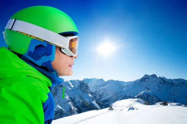 スノーボードのヘルメットで男の子の近い側の肖像は 高い山脈のピークの上に脇を見る — ストック写真
