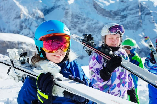 山の中でカラフルな衣装のマスクやヘルメットで子供たちの友人のグループと肩の上にスキーを保持女の子の肖像画 — ストック写真