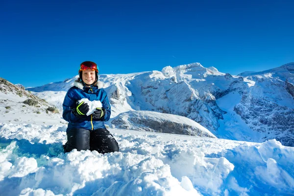 青い衣装のマスクとヘルメットショーの愛の概念を保持雪の形で心立って膝の上に山のピークと背景 — ストック写真