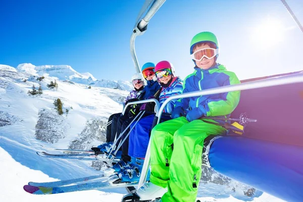 四个穿着鲜活滑雪服的快乐孩子在山上一起举着椅子 笑着的画像 — 图库照片