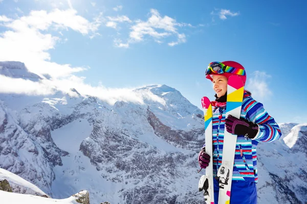 ピンクのヘルメットと色のスキーで笑顔かわいい女の子の肖像画 高い山のピークプロファイルビュー上でオフゴーグル — ストック写真
