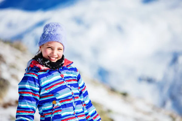 笑容可亲的女孩戴着滑雪帽 穿着彩色外套 高高兴兴地披着白雪覆盖的山前人像 — 图库照片