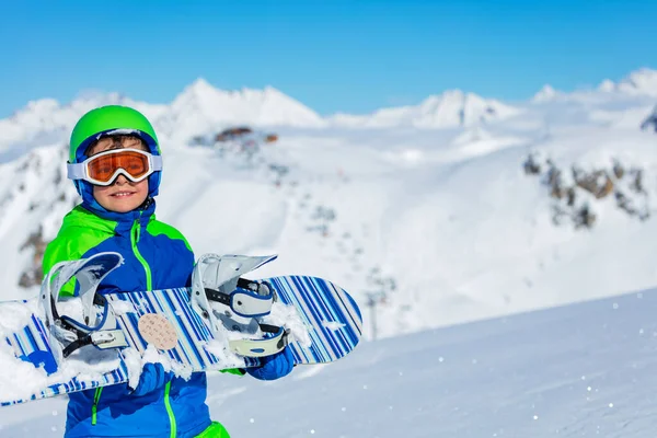 かわいい男の子は山の雪の冬のリゾートと背景にスキーリフトでスノーボードを保持します — ストック写真