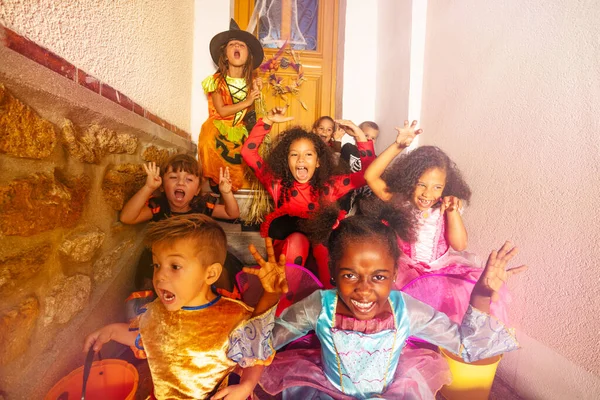 许多穿着万圣节服装的形式多样的孩子坐在屋子门口的楼梯上 — 图库照片