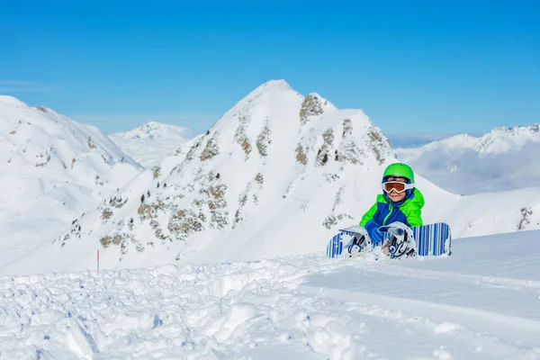 Portret Małego Snowboardzisty Siedzieć Śniegu Snowboardem Nad Górą Jasnoniebieskim Zielonym — Zdjęcie stockowe