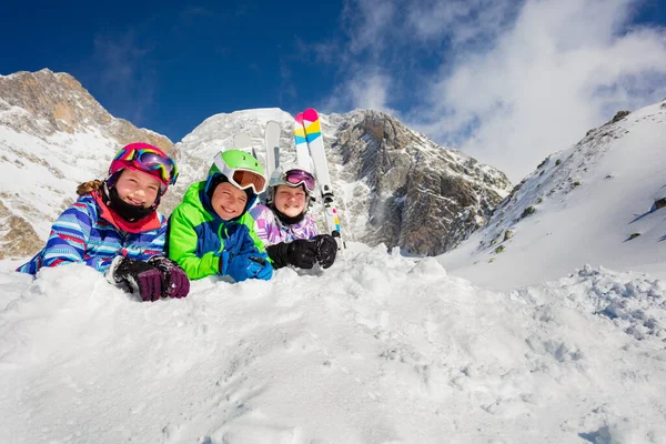 幸せな子供たちのグループは ヘルメットの上に行マスクの背景にスキーと雪の中で一緒に横たわって カメラを見て — ストック写真