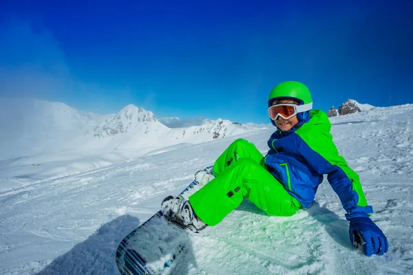 スノーボードの幸せな少年は フルスポーツ機器ヘルメットとマスクで雪の斜面に座っている — ストック写真