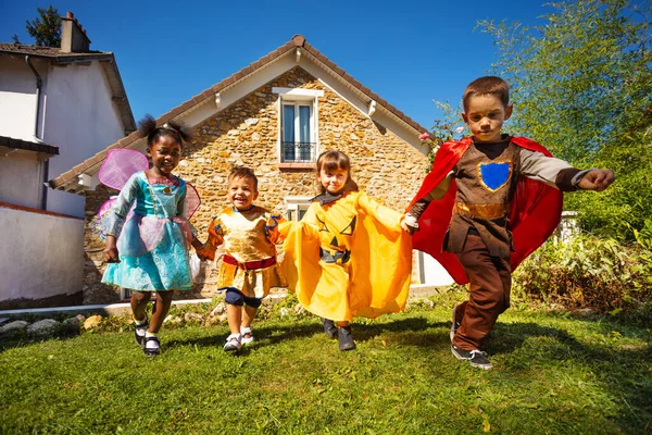 小さな子供たちのグループは 手を握って家の前に芝生の上でハロウィーンの衣装で実行されます — ストック写真