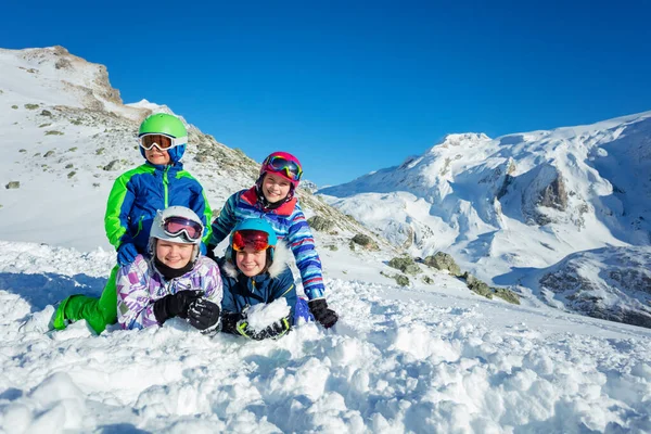 四个笑容满面的孩子们一起躺在雪地里 穿着山顶滑雪服 戴着彩色头盔和眼镜 — 图库照片