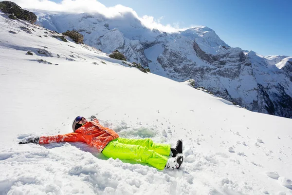 十代の女の子は山の中で高いオレンジ色の黄色いスキー服を着て雪の中で楽しい敷設を持っています — ストック写真