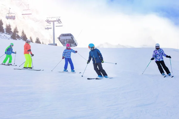 Class group of kids in ski school move one after another on Alpine slope learning